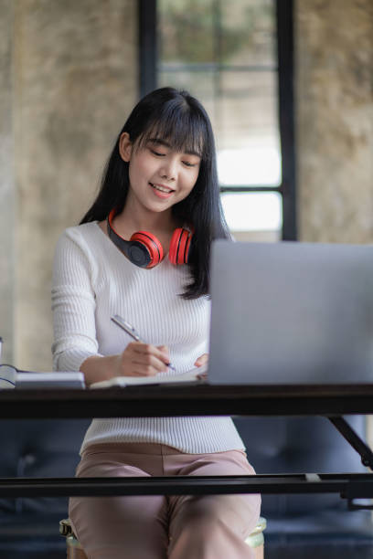 belle et joyeuse femme asiatique portant des écouteurs dans les vidéoconférences et les cours en ligne sur internet et appréciant d’écouter de la musique joyeusement sur son ordinateur portable de travail pendant les pauses de travail. - interview meeting business women photos et images de collection