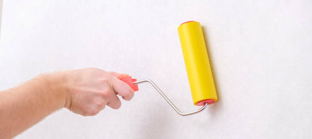 istock A man rolls out a canvas of white wallpaper with a suture wallpaper yellow roller. Removing air bubbles and glue from under the wallpaper. Wallpapering. 1440124404