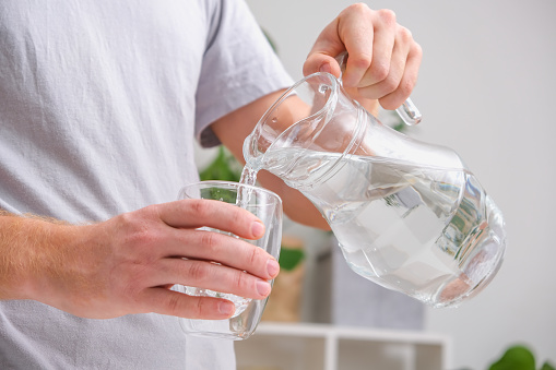 istock Man pours cold water into glass. Close-up of male hands pouring water from a jug into glass tumbler. 1440128467