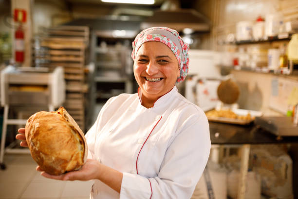 happy baker showing a loaf of bread - chef baker bakery flour imagens e fotografias de stock
