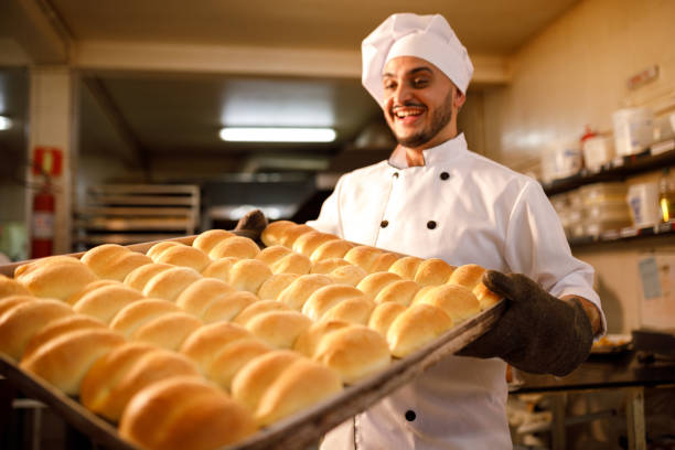 happy baker taking of a batch of baked bread from the oven - chef baker bakery flour imagens e fotografias de stock