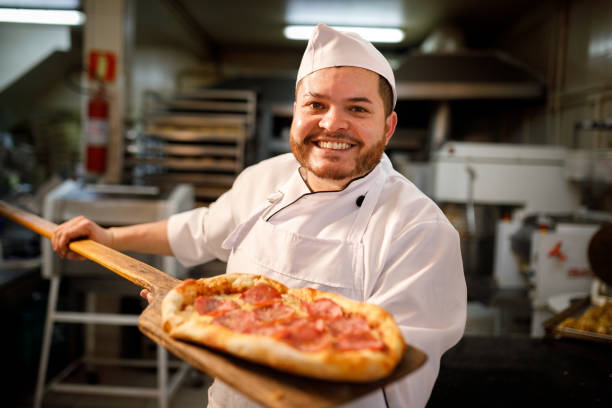 Portrait of happy attractive cook with a pizza in studio an a black background