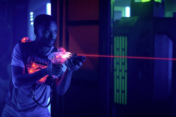 joueur de balise laser retenant la lumière de tir de canon dans le labyrinthe noir de lumière - gun men holding handgun photos et images de collection