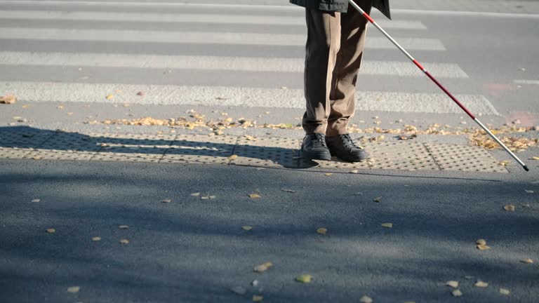 Lone blind man detecting tactile tiles, walking to pedestrian crossing safe road