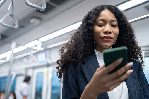 Young woman using cellphone with headset while taking the subway train to work at the rush hour morning.