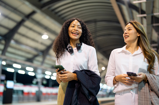 Two businesswomen stand and talk at the train station after work.