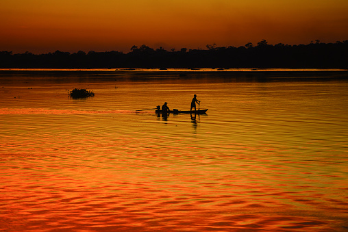 Silhouette of a man rowing a canoe at dusk on the Guaporé - Itenez river, Ricardo Franco village, Vale do Guaporé Indigenous Land, Rondonia state, Brazil