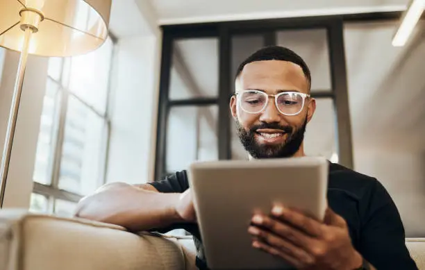 Photo of Black man, tablet and smile for social media post, shopping online or browsing internet creative content at home. Young africa american happy, relax and calm on tech digital app on device