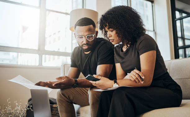 istock Laptop, communication and black couple with documents working on budget, savings plan or review mortgage bills. Financial paperwork, taxes and black woman and man planning finance banking payments 1440150999