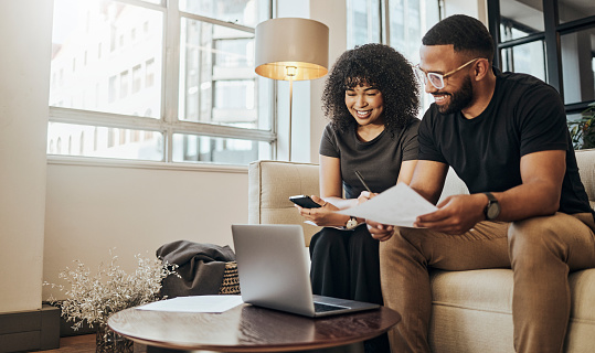 Happy, couple and laptop working with technology on living room sofa at home in paperwork, budget or finance. Black man and woman browsing phone for online banking, applications or mortgage payment