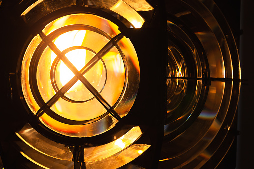 Glowing yellow lighthouse lamp with a Fresnel lens. It is a type of composite compact lens developed by the French physicist Augustin-Jean Fresnel for use in lighthouses