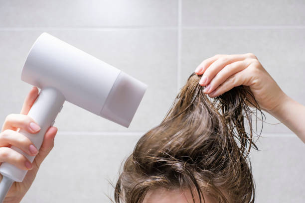 Young woman drying her hair with hairdryer in the bathroom close-up front view. stock photo