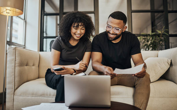 planificación, finanzas y acoplamiento con papel y portátil para presupuesto, seguro y ahorro en el sofá de su casa. feliz, joven y hombre y mujer aprendiendo sobre inversión en línea y préstamo con documentos - loan fotografías e imágenes de stock