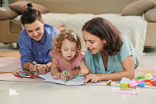 Joyful lesbian couple and their little daughter coloring pictures together