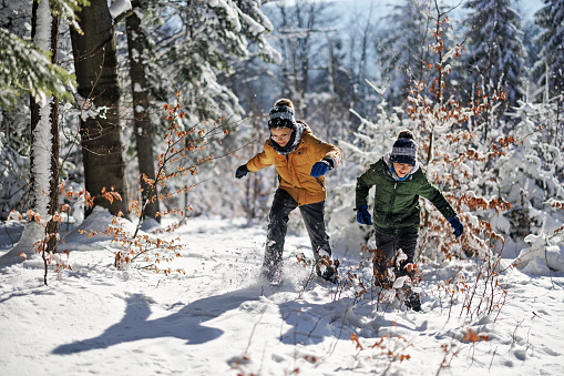 Kids running through snowy forest. Boys are having fun on a cold winter day.\nCanon R5