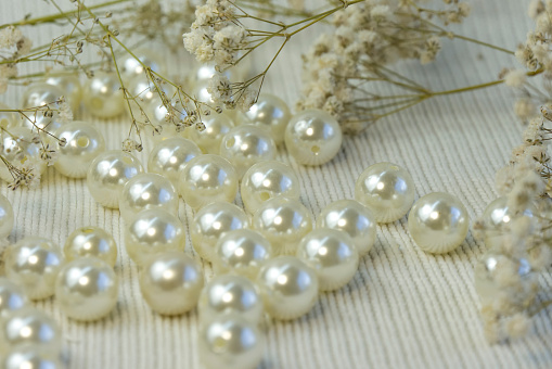 Bright beautiful whitw pearl beads scattered on white knitted textured background, close up top view
