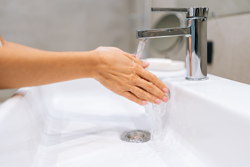 Close-up cropped shot of unrecognizable female washing hands with soap and hot water at home bathroom sink for help fight bacteria and germs in bath with light interior. Concept of healthy lifestyle.