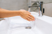 Close-up cropped shot of unrecognizable female washing hands with hot water at home bathroom sink for help fight bacteria and germs in bath with light interior.