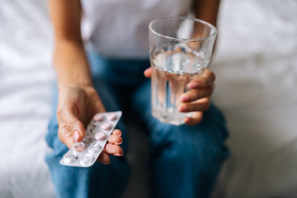 Close-up high-angle view of unrecognizable young woman holding pill in hand with water. Female going to take tablet from headache, painkiller. Close-up high-angle view of unrecognizable young woman holding pill in hand with water. Female going to take tablet from headache, painkiller, medication drinking clear water from glass, cropped shot. sleeping pill stock pictures, royalty-free photos & images