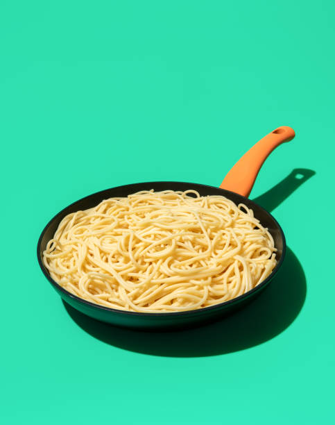 Iron cast pan with cooked spaghetti minimalist on a green table. Pasta without any sauce or condiments in a frying pan.