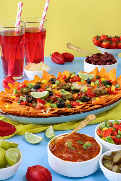 istock Full frame image of homemade, loaded nachos covered in melted mozzarella cheese, cherry tomatoes, black olives, Jalapeno peppers, elevated view, focus on foreground, served with sauces and dips 1440160804