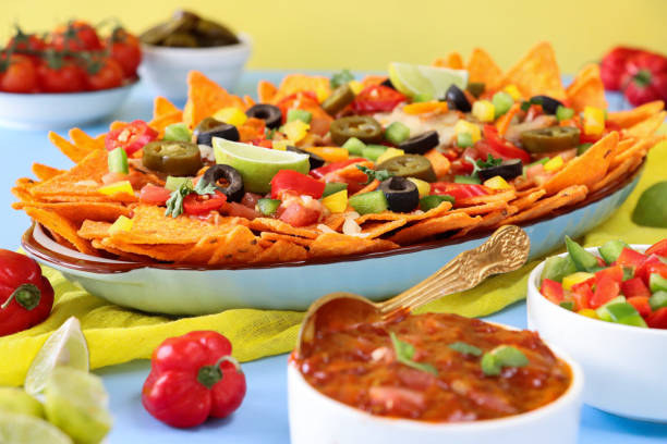 istock Full frame image of homemade, loaded nachos covered in melted mozzarella cheese, cherry tomatoes, black olives, Jalapeno peppers, elevated view, focus on foreground, served with sauces and dips 1440160805