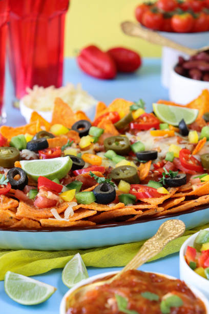 istock Full frame image of homemade, loaded nachos covered in melted mozzarella cheese, cherry tomatoes, black olives, Jalapeno peppers, elevated view, focus on foreground, served with sauces and dips 1440160808