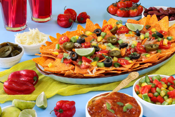 istock Full frame image of homemade, loaded nachos covered in melted mozzarella cheese, cherry tomatoes, black olives, Jalapeno peppers, elevated view, focus on foreground, served with sauces and dips 1440160809