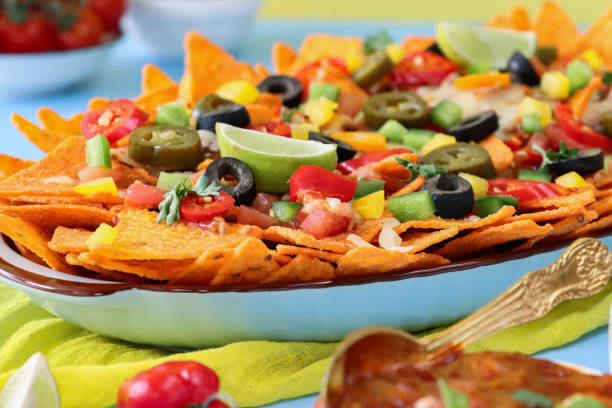 istock Full frame image of homemade, loaded nachos covered in melted mozzarella cheese, cherry tomatoes, black olives, Jalapeno peppers, elevated view, focus on foreground, served with sauces and dips 1440160820
