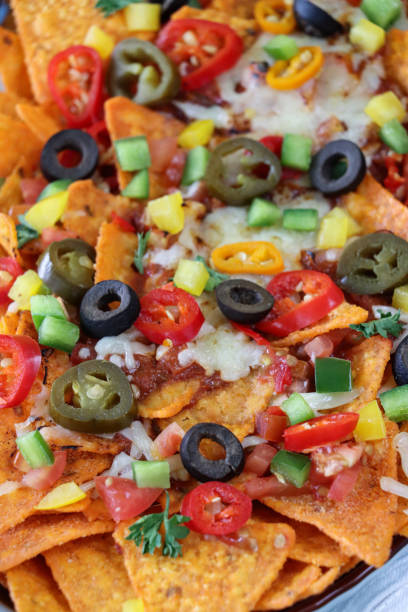 istock Full frame image of homemade, loaded nachos covered in melted mozzarella cheese, cherry tomatoes, black olives, Jalapeno peppers, elevated view, focus on foreground 1440160831