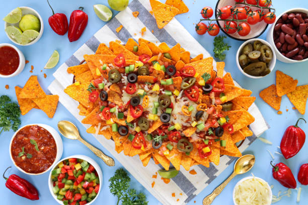 istock Full frame image of homemade, loaded nachos covered in melted mozzarella cheese, cherry tomatoes, black olives, Jalapeno peppers, elevated view, focus on foreground, served with sauces and dips 1440160834