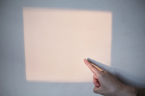 finger pointing at a sunlight shadow on a wall