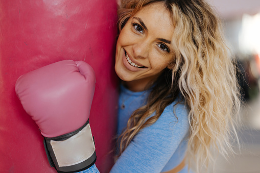Close-up shot of young female boxer hugging punching bag and smiling at camera