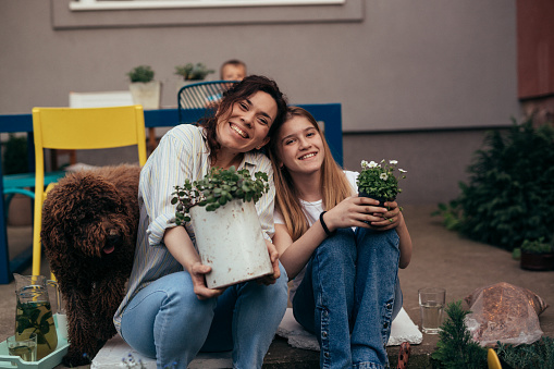 happy mother and daughter holding plants and looking at camera