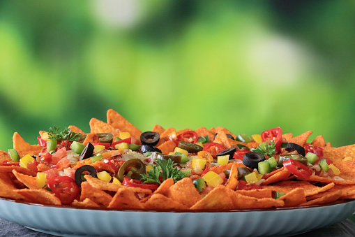 Stock photo showing close-up view of homemade loaded nachos recipe. This snack contains fresh, crunchy tortilla chips covered with tomato salsa and melted cheese with chopped tomatoes, black olives, green and yellow bell peppers, Jalapeno peppers and red chillies.