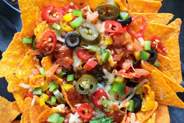 istock Full frame image of homemade, loaded nachos covered in melted mozzarella cheese, cherry tomatoes, black olives, Jalapeno peppers, elevated view, focus on foreground, served with sauces and dips 1440166377