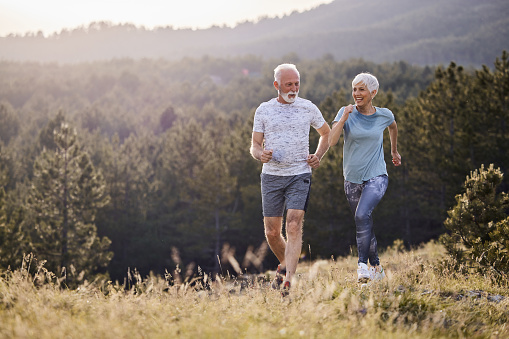 Happy mature couple running in nature. Copy space.