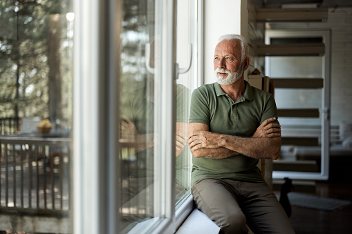 Mature man relaxing by the window with his arms crossed and day dreaming.