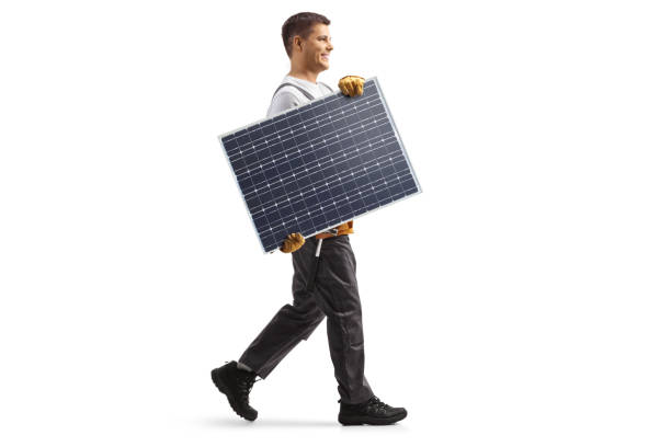 Full length profile shot of a technician carrying a solar panel and walking stock photo