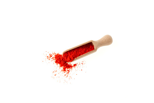Red pepper ground in wooden scoop on white background, top view. Dried Red Chili Pepper or Paprika powder.