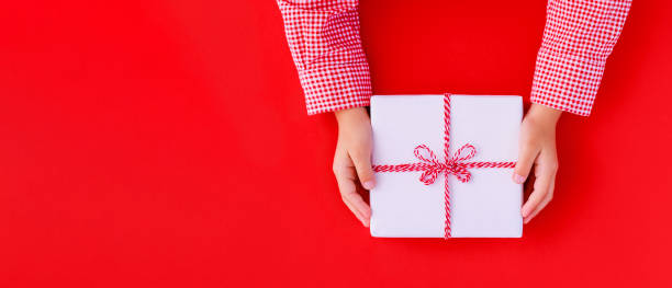 istock Christmas banner gift box in children's hands on a red background, presenting a gift 1440178083