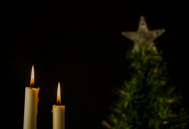 Light of white candles with Christmas tree against black background