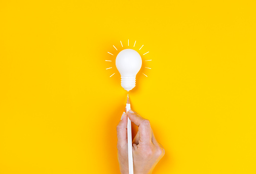 Female hand pointing to light bulb with white pen. Business creativity and inspiration concepts on yellow background.