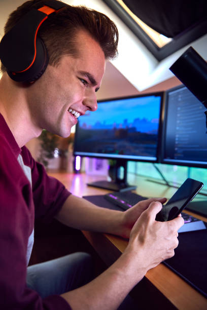 istock Man With Mobile Phone Gaming At Home Sitting At Desk With Multiple Monitors 1440183100