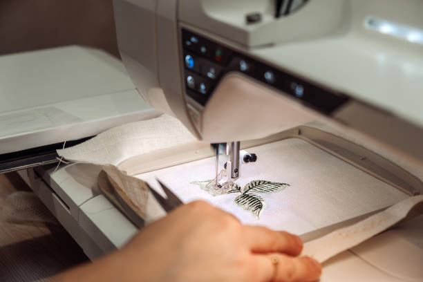 Female tailor makes embroidery on an embroidery machine in a home workshop,hands close-up.Mending clothes concept,small business. stock photo