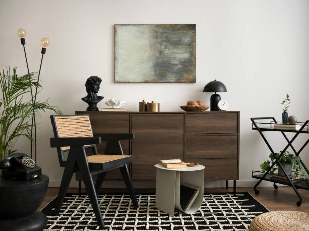 istock Creative compostion of living room interior with mock up poster frame, plants, patterned rug, lamp, wooden commode, rattan chair, stylish coffee table and personal accessories. Home decor. Template. 1440184060