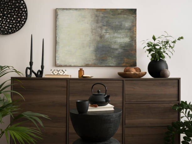 istock Interior design of living room interior with mock up poster frame, wooden commode, black candlestick, coconut, vase with dried flowers and personal accessories. Home decor. Template. 1440184065
