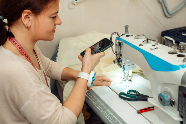 Caucasian woman tailor sews on a sewing machine in a home workshop and records the broadcast on a smartphone.Small business.Blogging concept Caucasian woman tailor sews on a sewing machine in a home workshop and records the broadcast on a smartphone.Small business.Blogging concept. machine sewing white sewing item stock pictures, royalty-free photos & images
