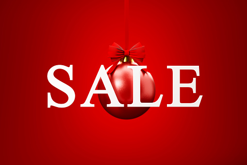 Sale sign over red Christmas bauble on red background. Horizontal composition with copy space. Front view. Great use for Christmas Sale concepts.