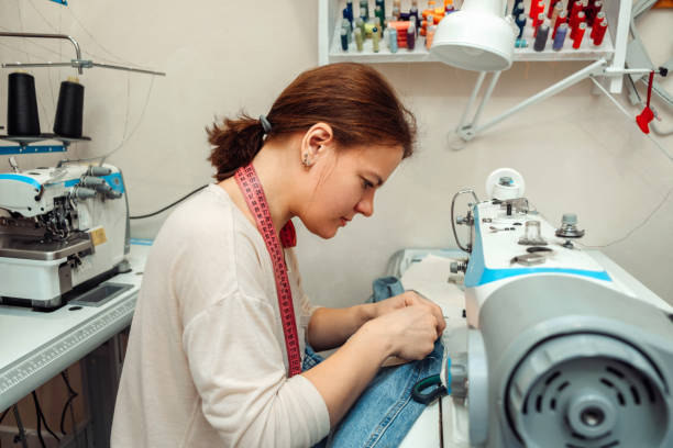 A woman mends jeans, sews a patch on a hole in the home studio.Mending clothes concept,reusing old jeans.Small business stock photo